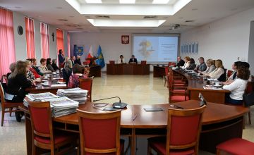 Sala sesyjna przystołach po prawej i lewej stronie siedzą zebrani na konferencji goście